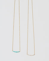 Closeup detail of the Opal Crescent Necklace and Turquoise Crescent Necklace on light color background.