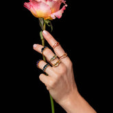 product_details::Styled image of Rainbow Rings on worn on a hand holding a flower.