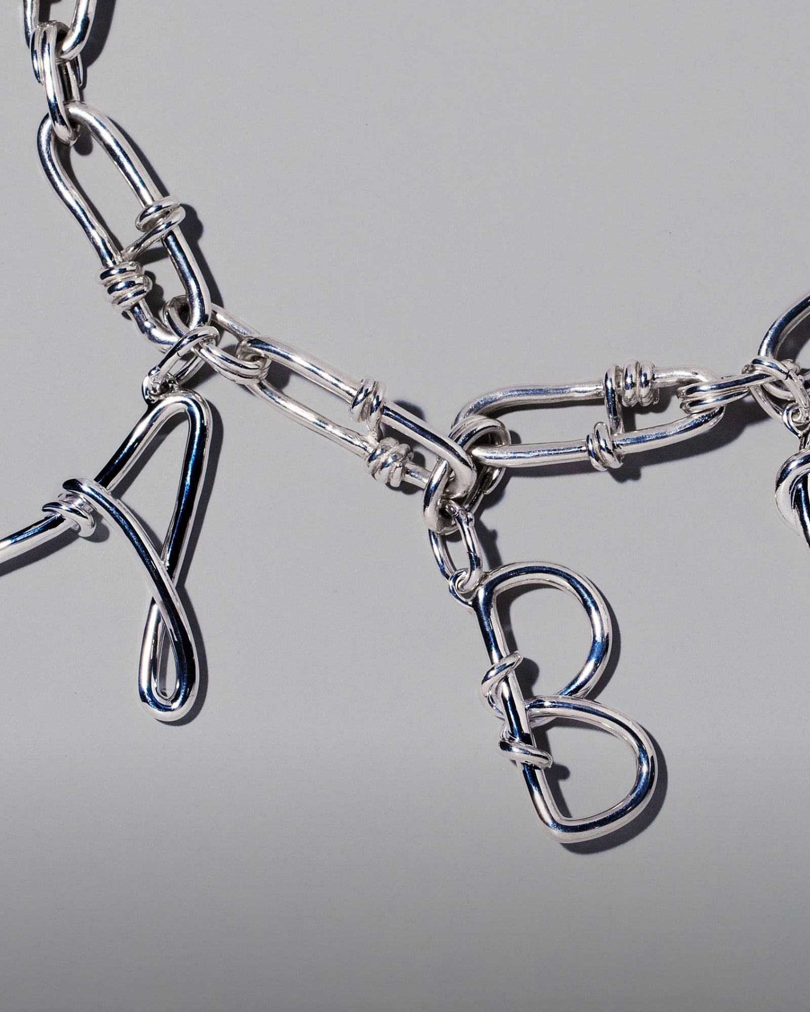 CRZM Large Sterling Silver Letter Charm A, CRZM Large Sterling Silver Letter Charm B and CRZM Sterling Silver Canyon Necklace on light color background.