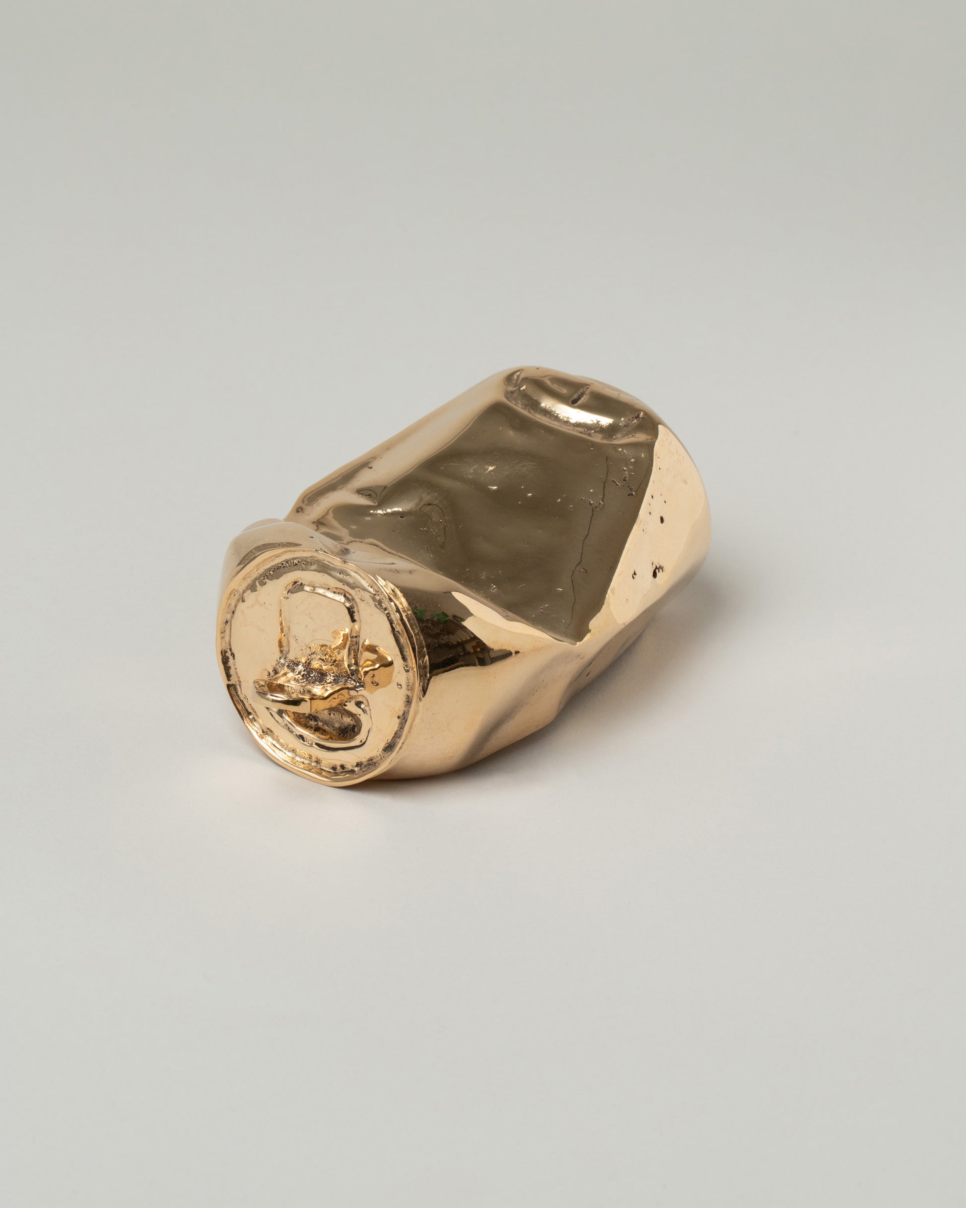 View from the side of the Pearce Objects Cast Bronze Crushed Can on light color background.