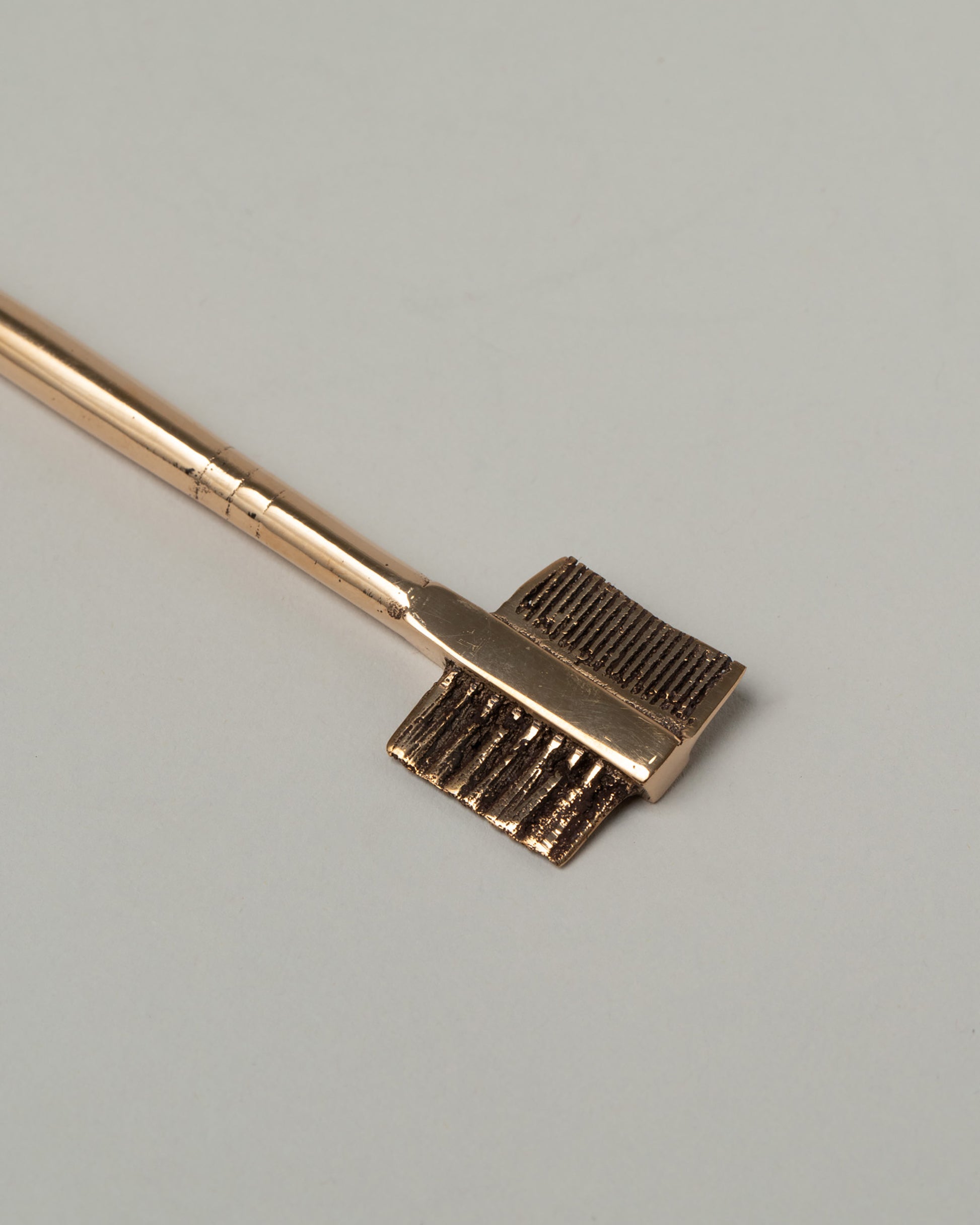 Closeup details of the Pearce Objects Cast Bronze Eyebrow Brush on light color background.