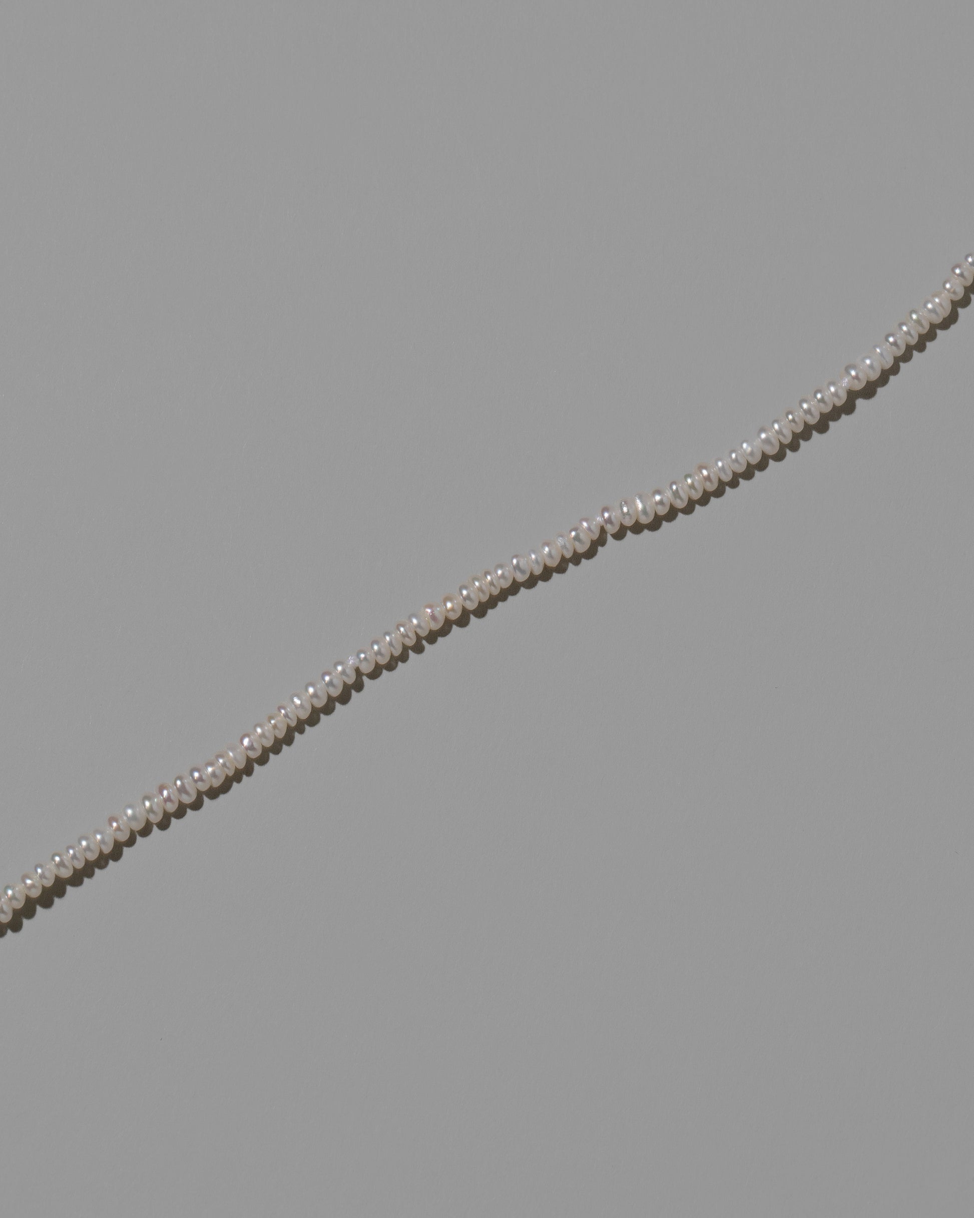 Closeup details of the White Pebble Seed Pearl Anklet on light color background.