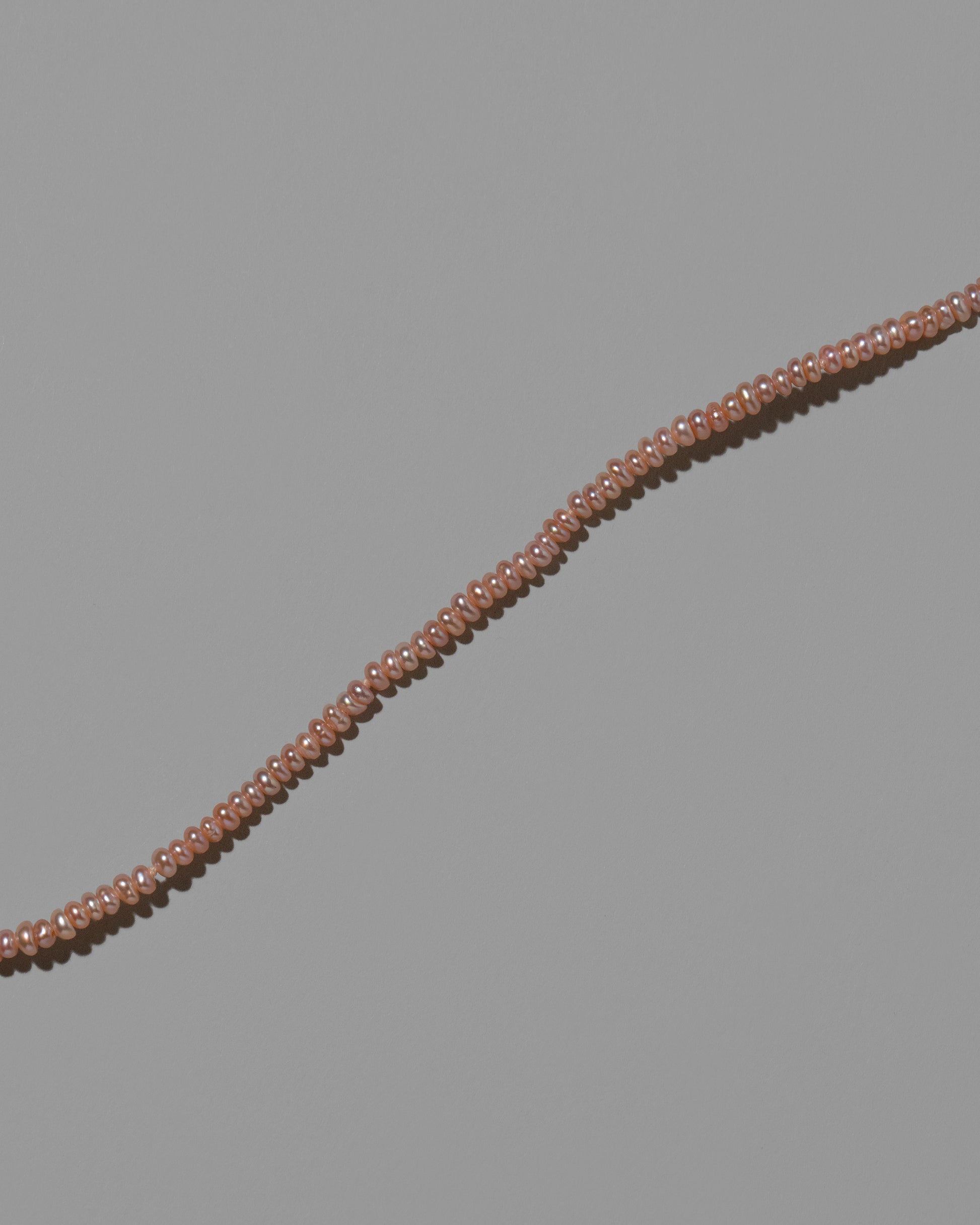 Closeup details of the Pink Seed Pearl Anklet on light color background.