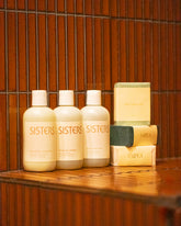 Styled image featuring the Sisters Body Gentle Body Wash, Balancing Shampoo and Nourishing Conditioner and Saipua Saltwater, Vetiver with French Green Clay, Black Soap with Charcoal and Patchouli bar soaps.