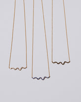 Closeup details of a group of Blue Sapphire, Black Diamond and White Diamond Ripple Wave Necklaces on light color background.