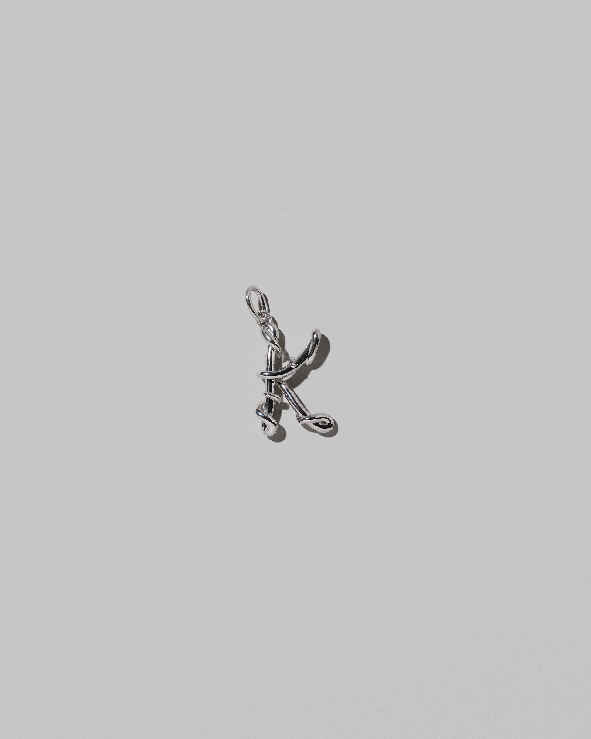 CRZM Medium Letter K Charm set in sterling silver on light color background.
