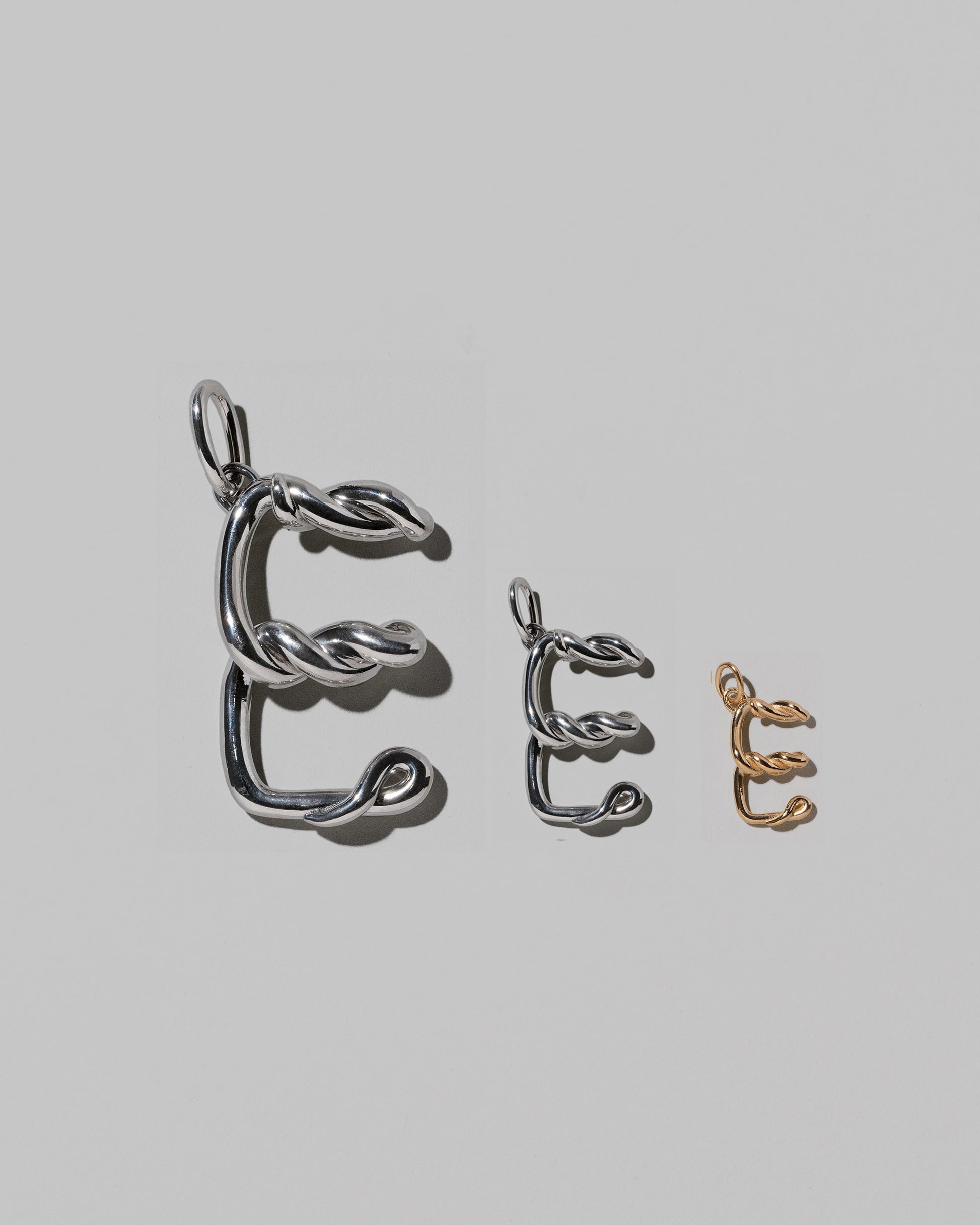 CRZM Large Sterling Silver, Medium Sterling Silver & Mini Letter E Charms set in solid gold on light color background.