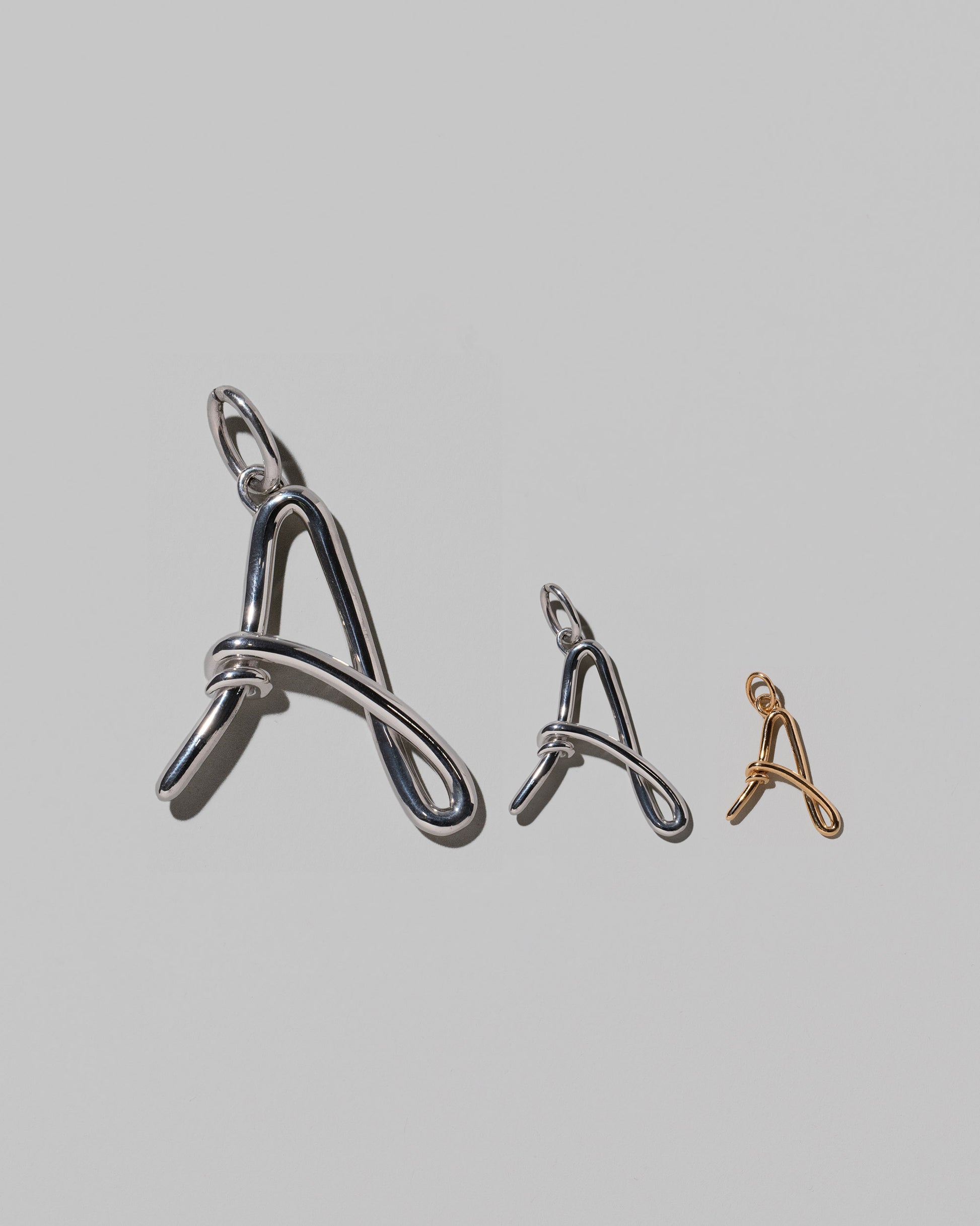 CRZM Large Sterling Silver, Medium Sterling Silver & Mini Letter A Charms set in solid gold on light color background.