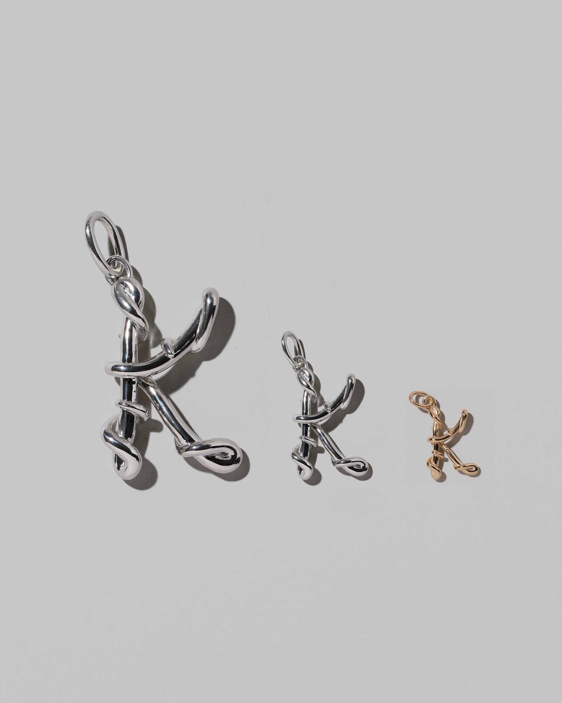 CRZM Large Sterling Silver, Medium Sterling Silver & Mini Letter K Charms set in solid gold on light color background.