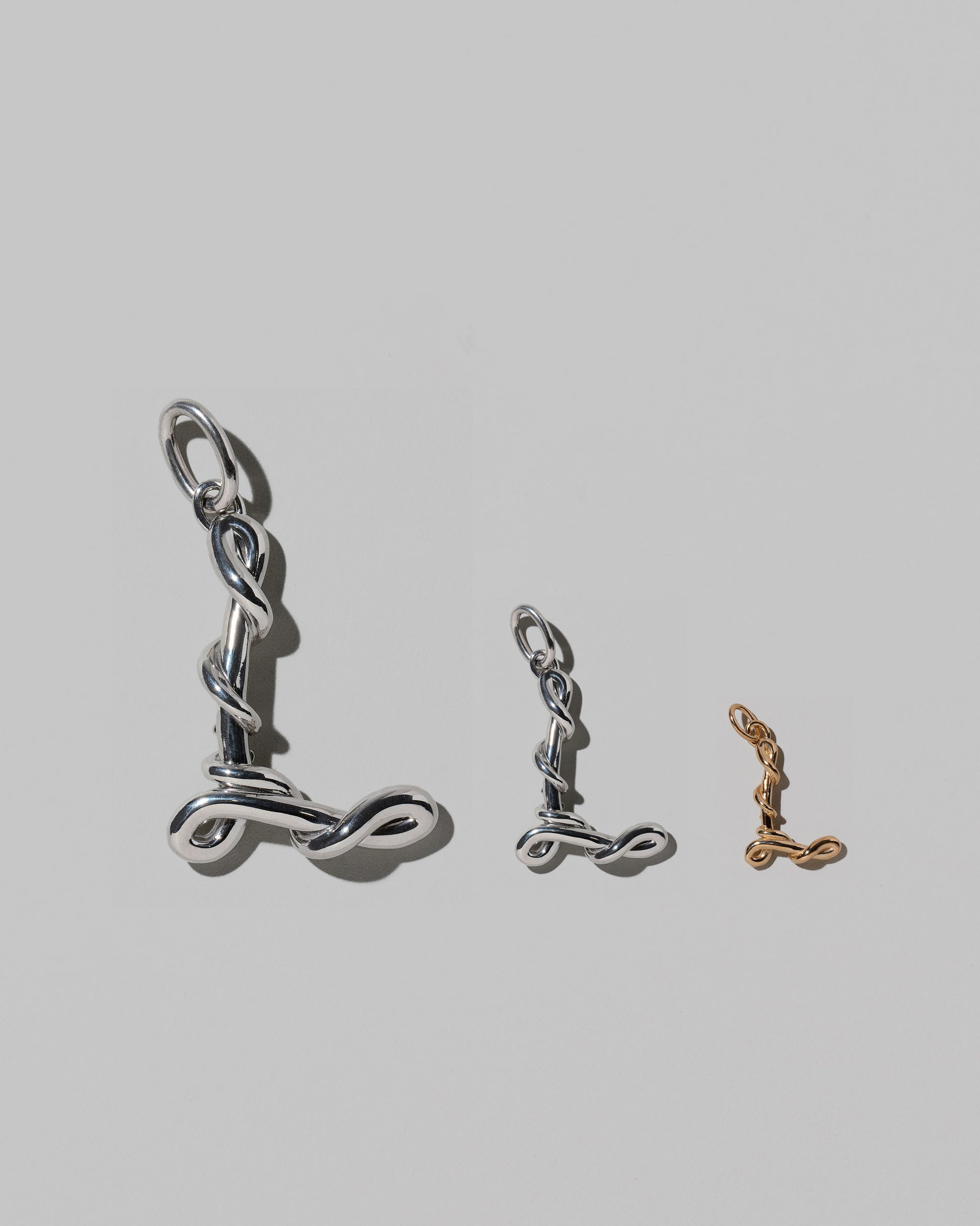 CRZM Large Sterling Silver, Medium Sterling Silver & Mini Letter L Charms set in solid gold on light color background.