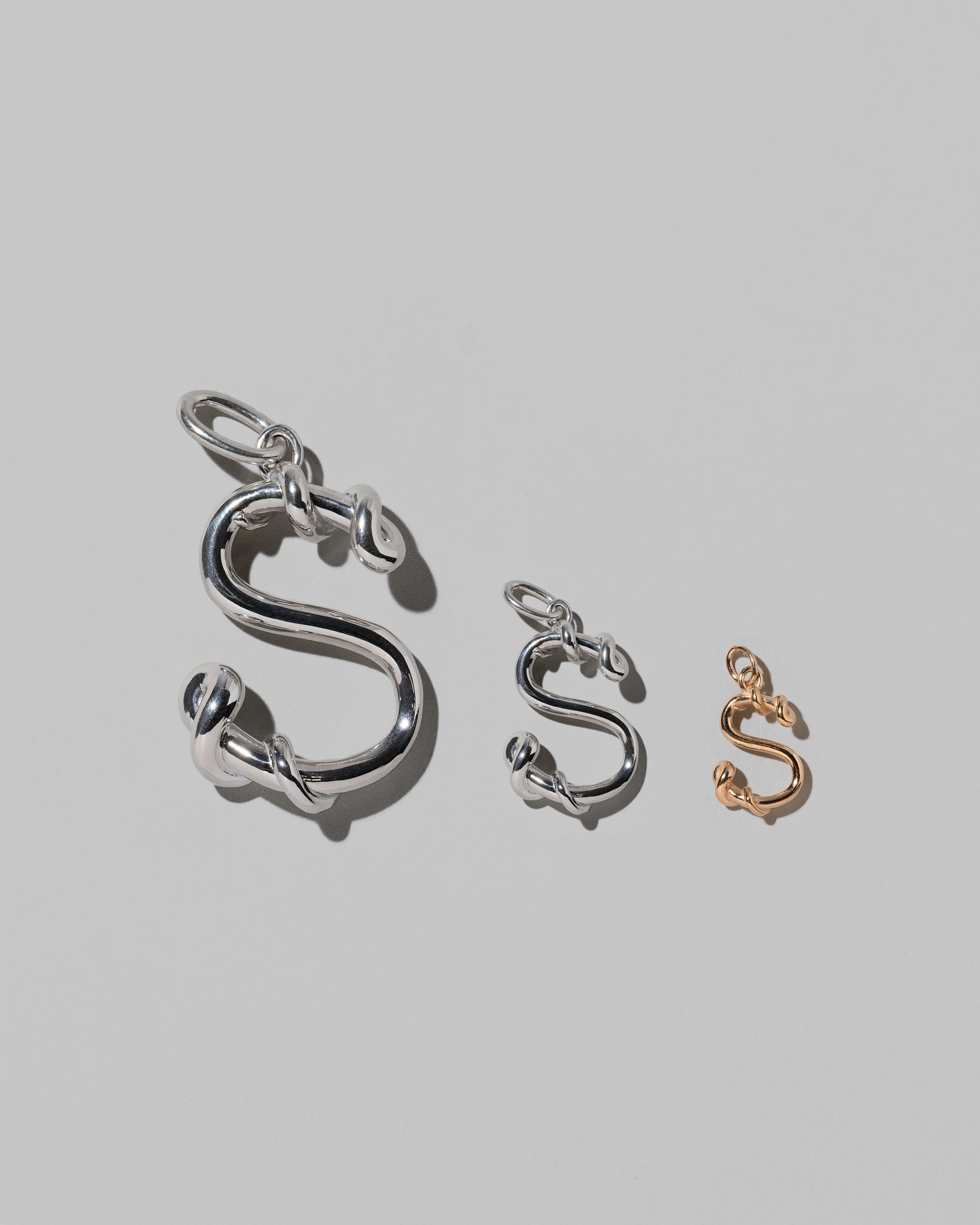 CRZM Large Sterling Silver, Medium Sterling Silver & Mini Letter S Charms set in solid gold on light color background.