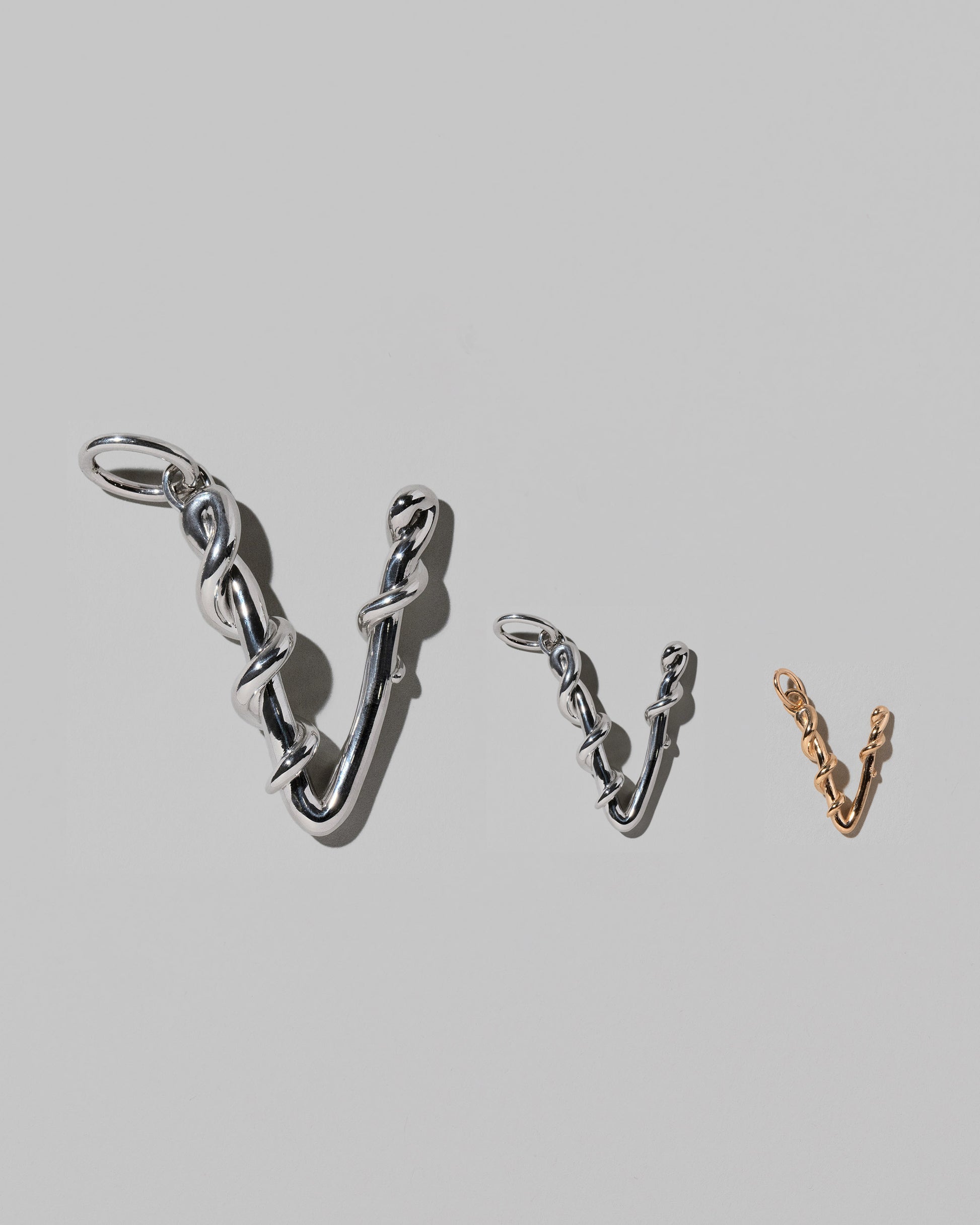 CRZM Large Sterling Silver, Medium Sterling Silver & Mini Letter V Charms set in solid gold on light color background.