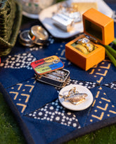 Styled image of the Sardine Can Charm, with the Luna Ring Charm, Salted Butter Charm, California Poppy Charm, Daffodil Charm, Sardine Fish Charm and Saltine Charms.