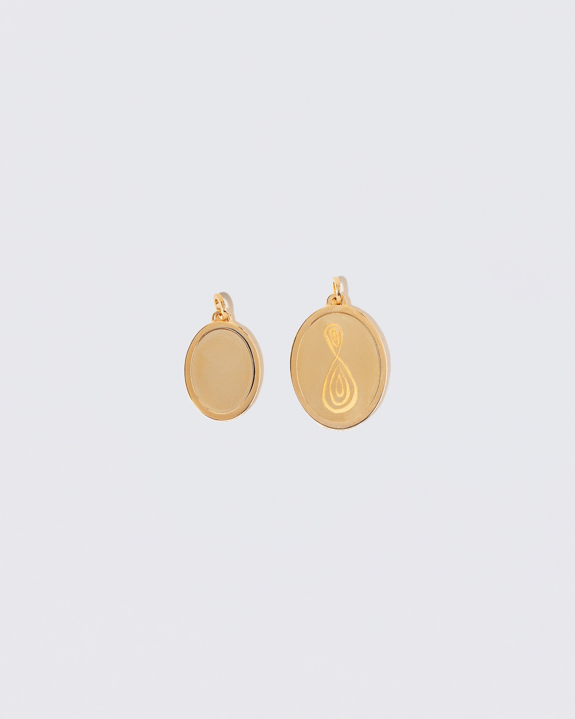 Unfinished Small Oval Pendant Memento Pendant and a finished Large Oval Pendant Memento Pendant engraved with an abstract isymbol on light color background.