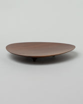 View from the side of the Namu Home Goods Black Walnut Asymmetrical Footed Plate on light color background.