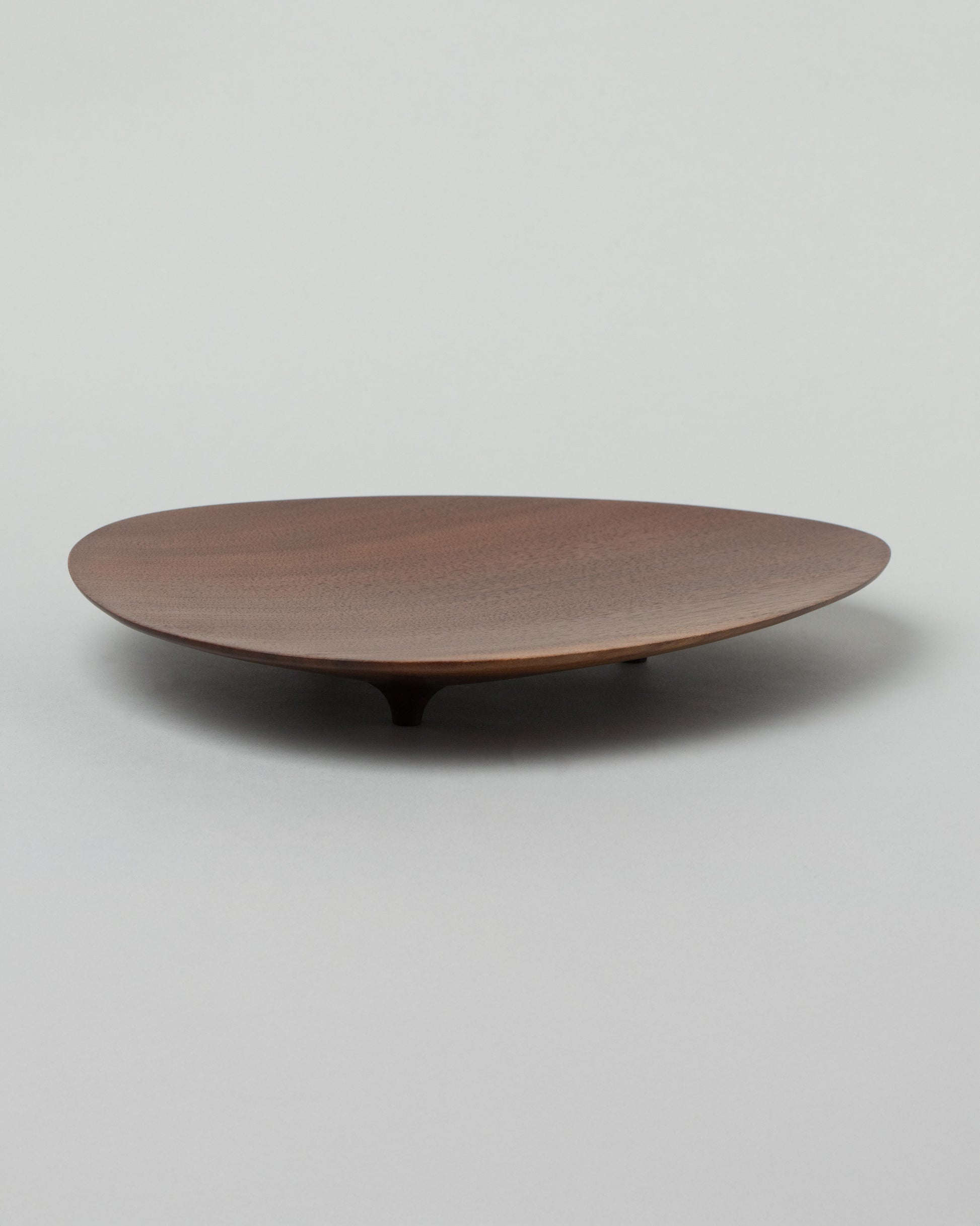 View from the side of the Namu Home Goods Black Walnut Asymmetrical Footed Plate on light color background.