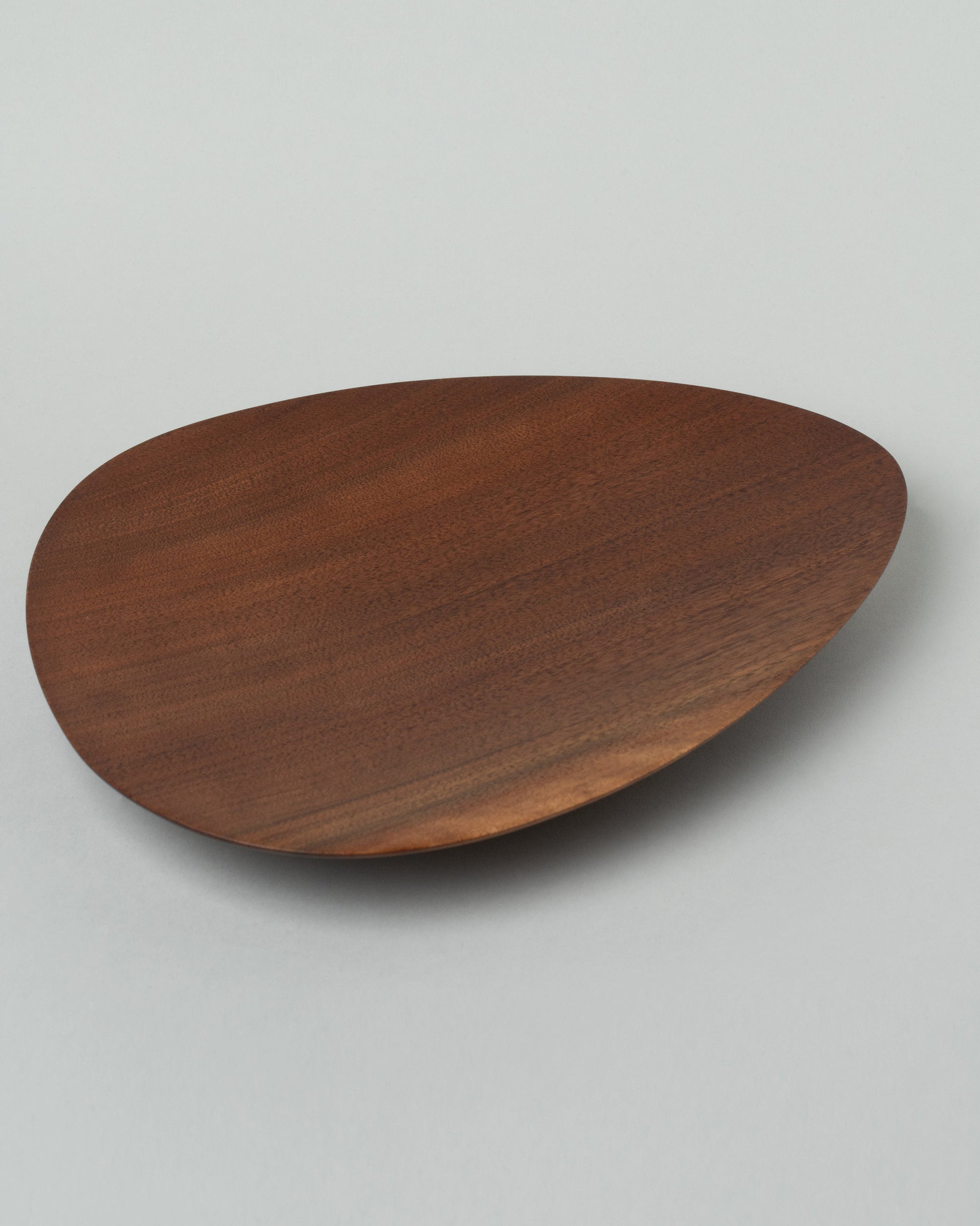 Closeup details of the Namu Home Goods Black Walnut Asymmetrical Footed Plate on light color background.