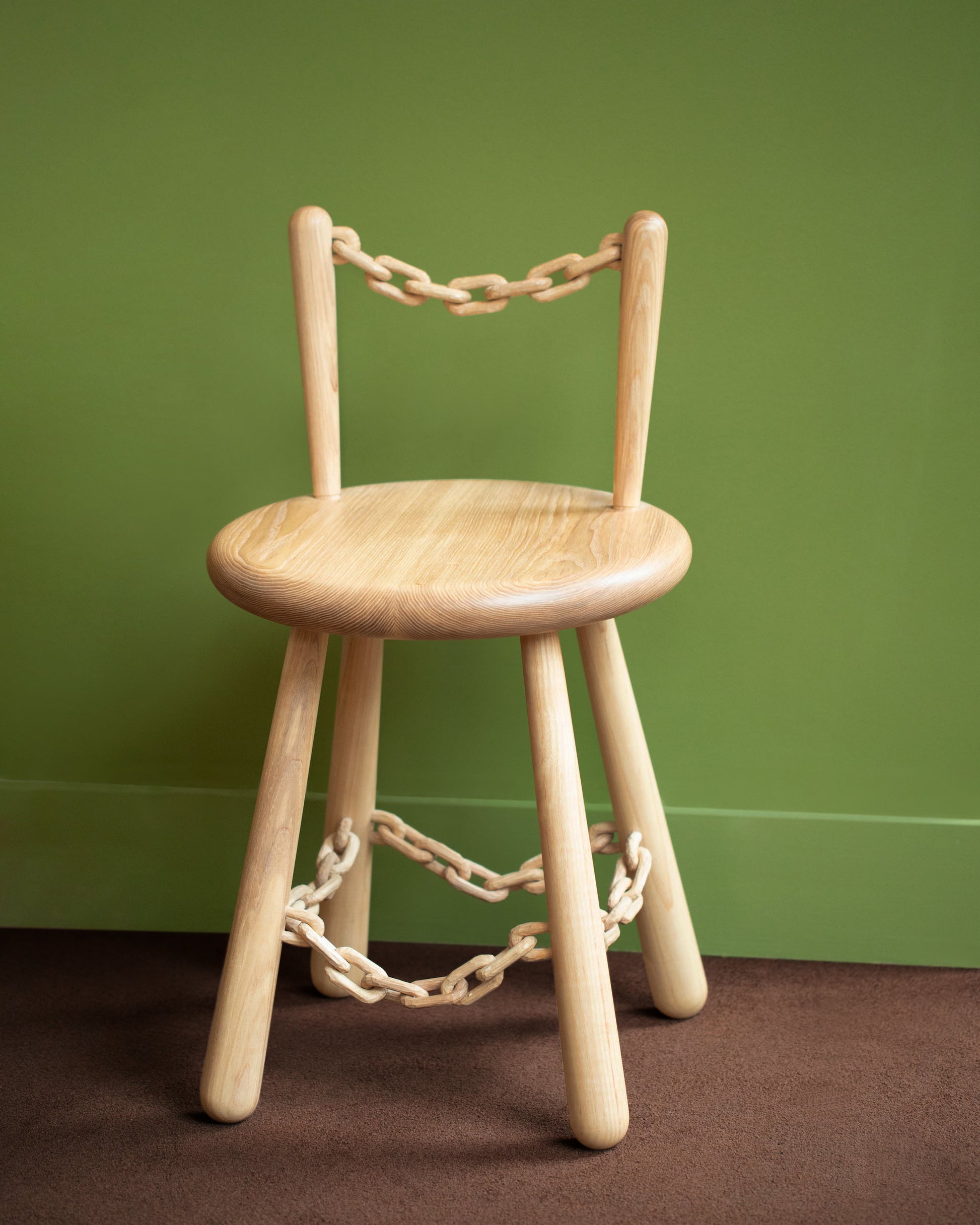 View from the side of the Pat Kim Chain Chair One on green color background.