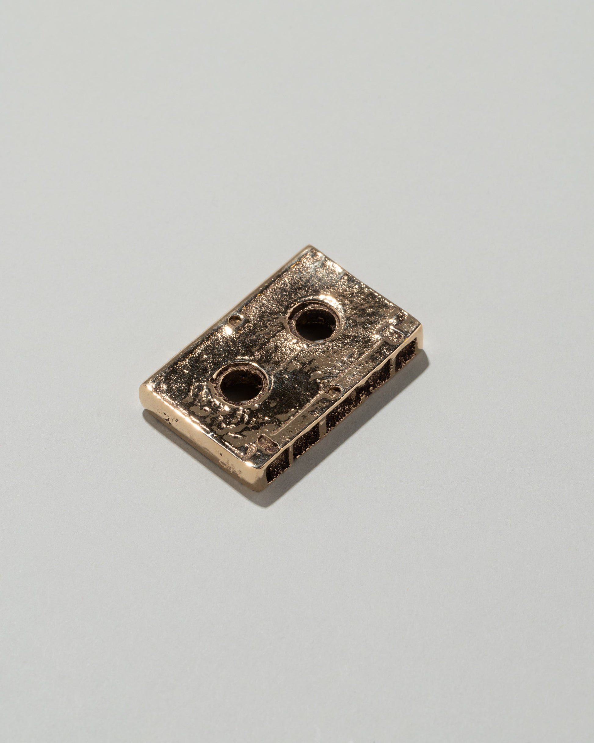 Closeup details of the Pearce Objects Cast Bronze Mini Cassette Tape on light color background.