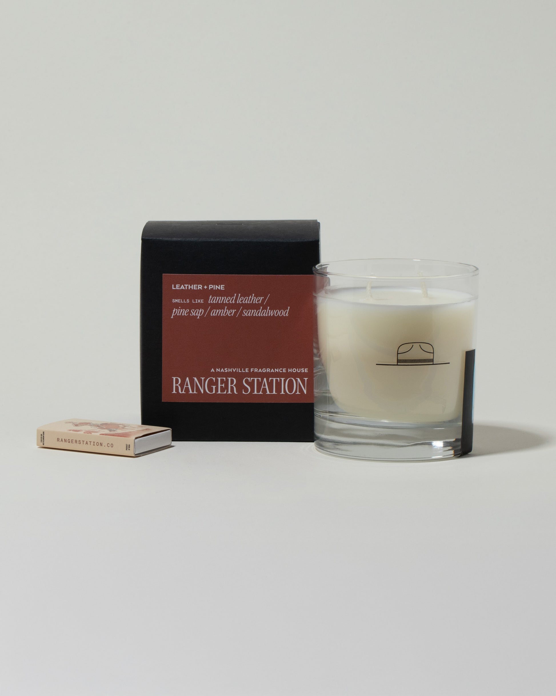 Ranger Station Leather & Pine Candle with matchbox on light color background.