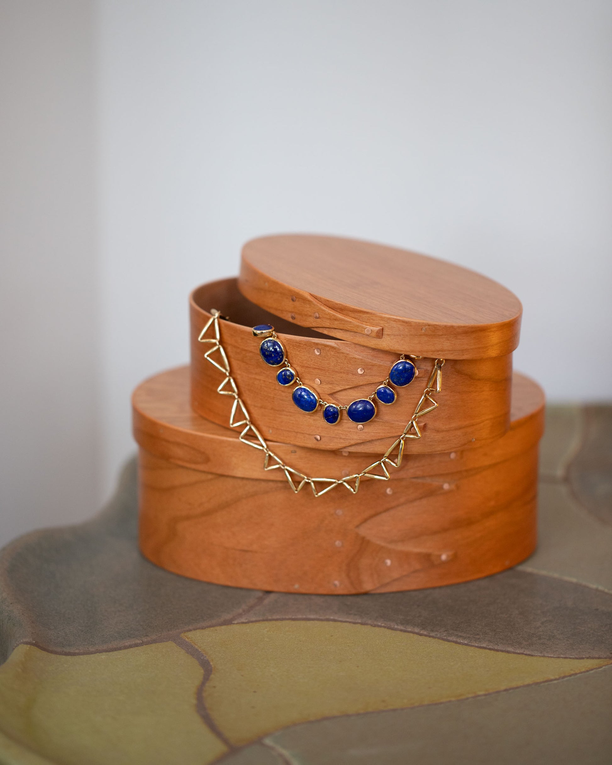 Styled image featuring the Rikke Falkow Extra Small and Small Cherry Wood Oval Boxes, with the Apparition Necklace and Gold Flexure Necklace.