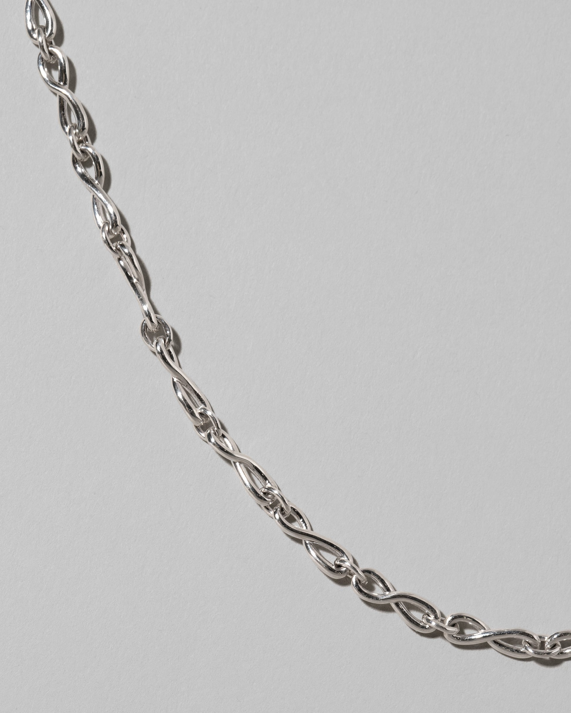 Closeup details of the CRZM Sterling Silver Infinity Chain Necklace on light color background.