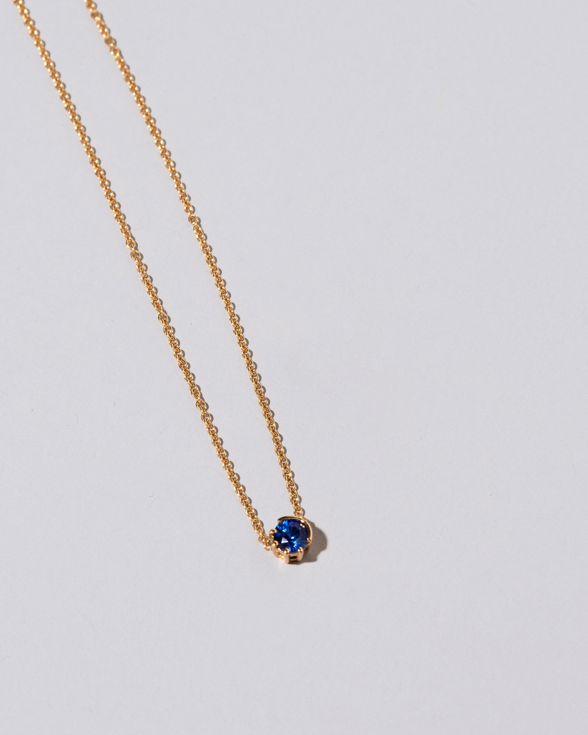 Closeup view of the Sapphire Sun & Moon Necklace on light color background.