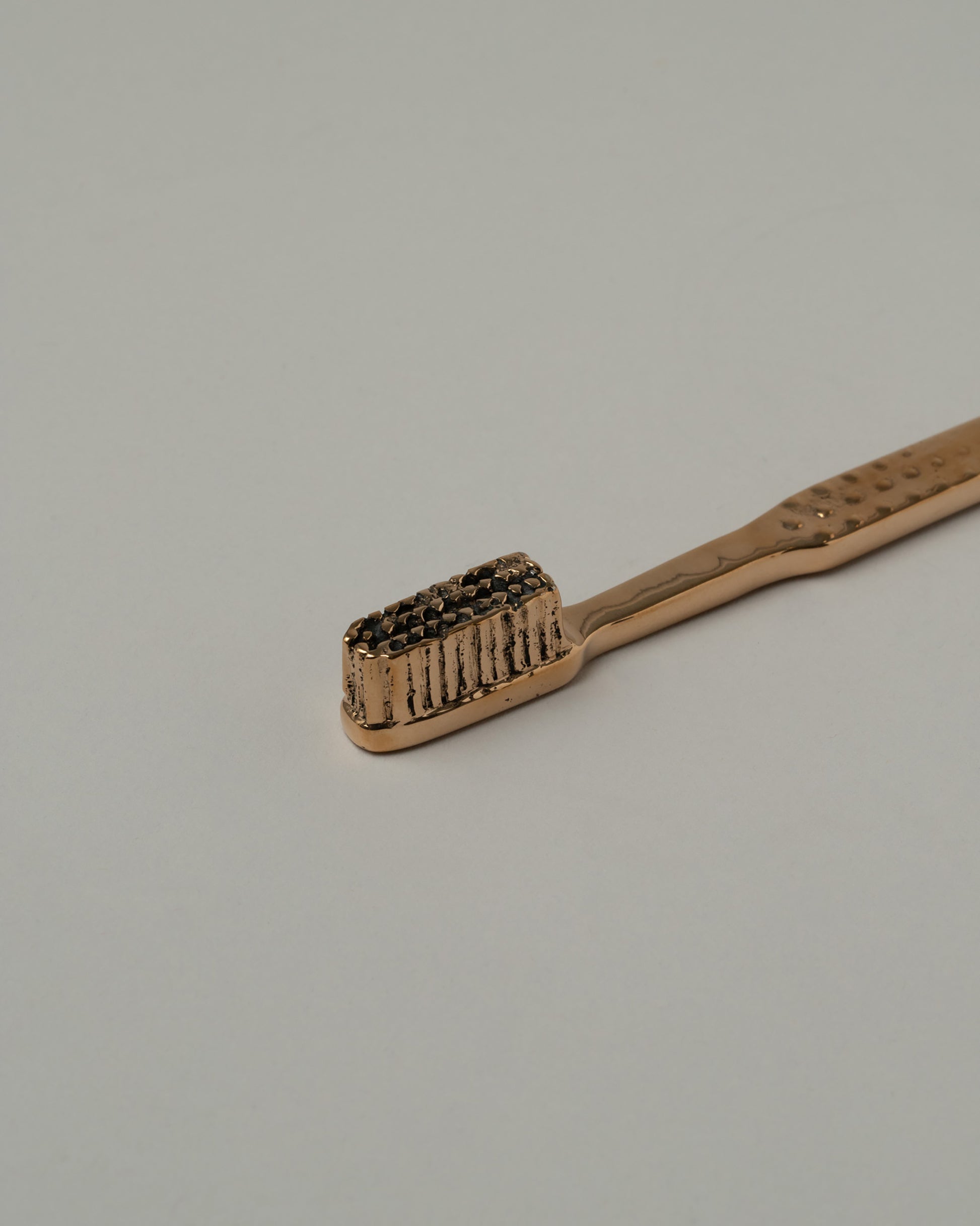 Closeup details of the Pearce Objects Cast Bronze Toothbrush on light color background.
