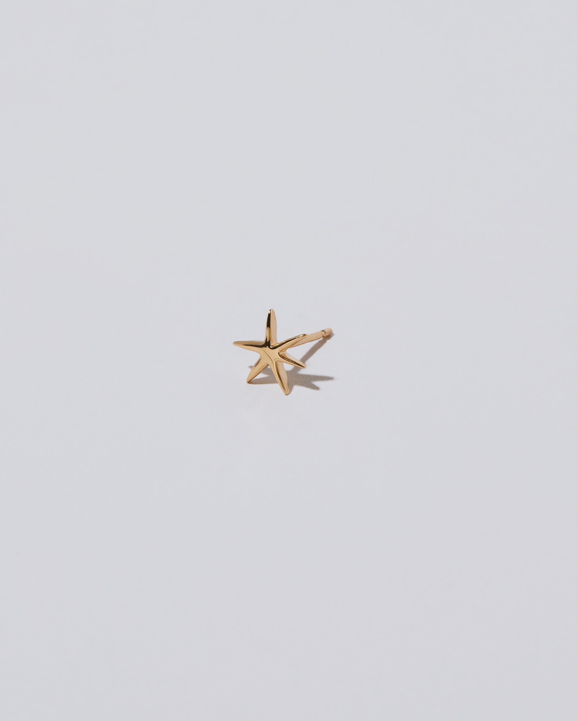 View from the side of the Shape Two Small Verve Six Point Star Stud Earring single on light color background.