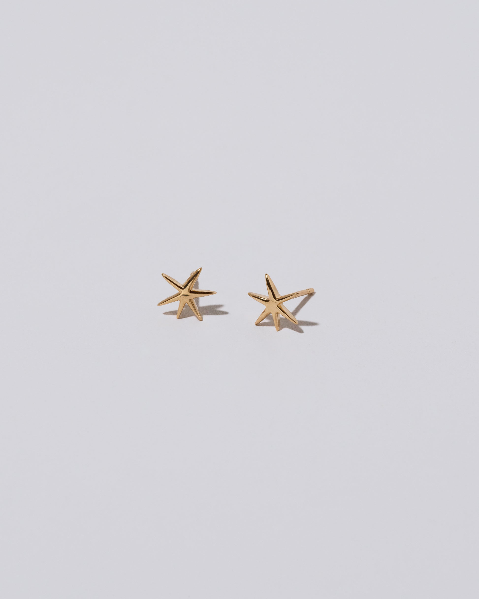 Closeup details of Shape Two Small Verve Six Point Star Stud Earrings on light color background.