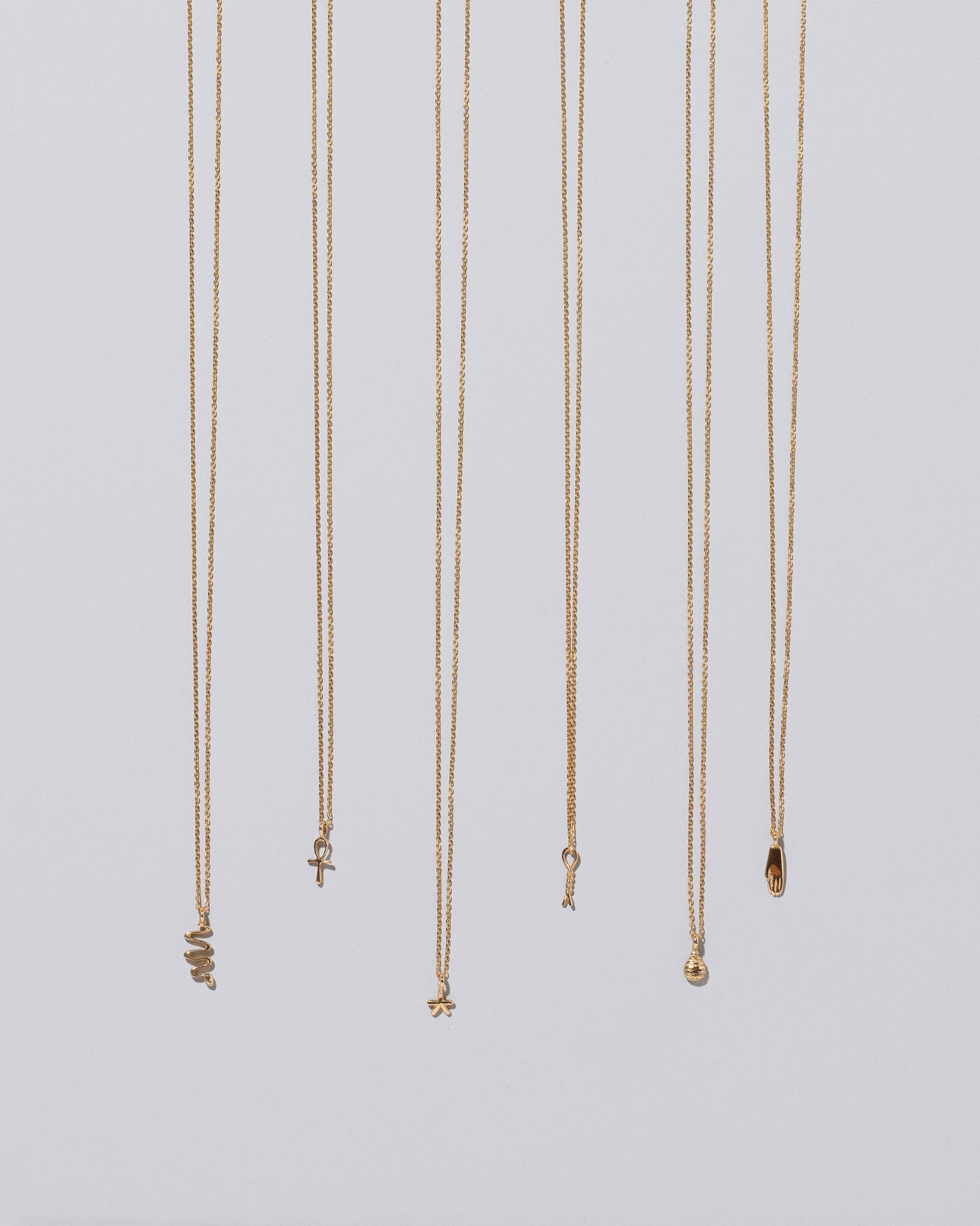 Group of Ankh, Star, Twist, Tear, Hand and Snake Talisman Pendant Necklaces on light color background.