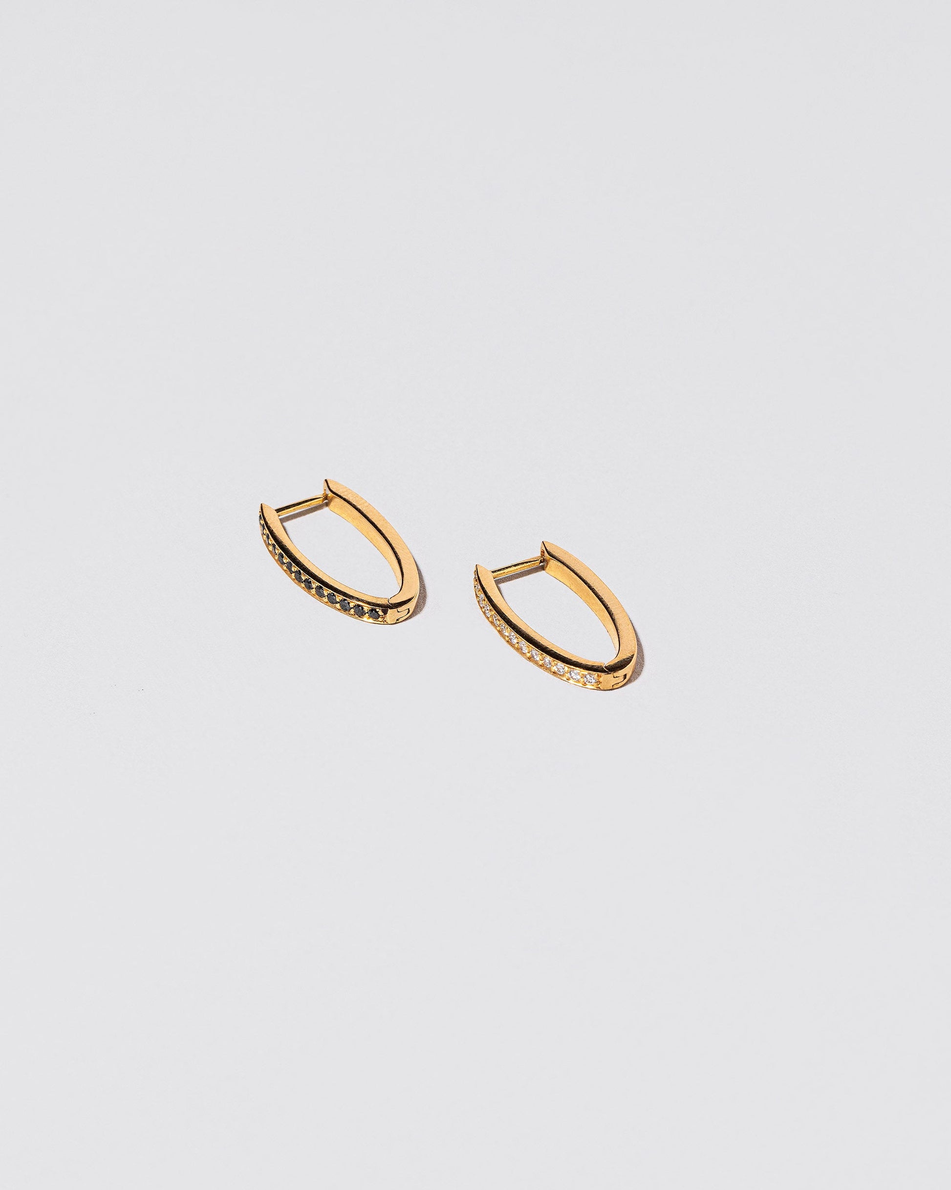 View from the side of the Gold Mismatch Black & White Diamond Tiny Loop Hoop Earrings on light color background.