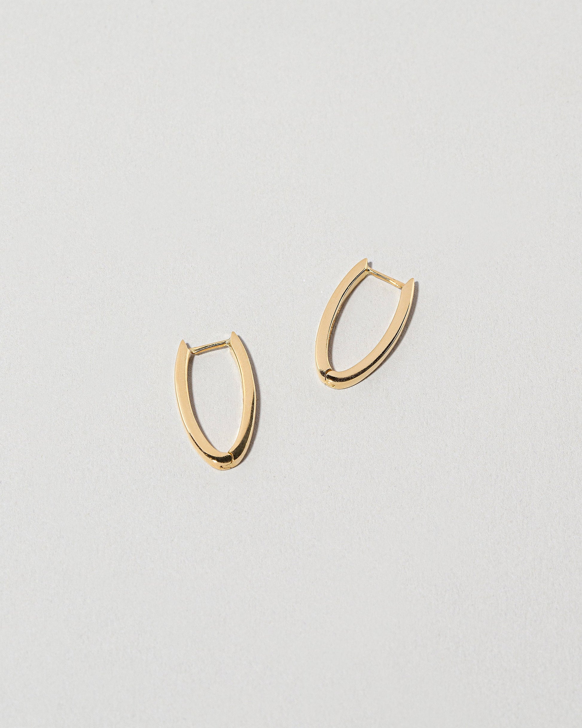 Closeup details of the Gold Solid Tiny Loop Hoop Earrings on light color background.