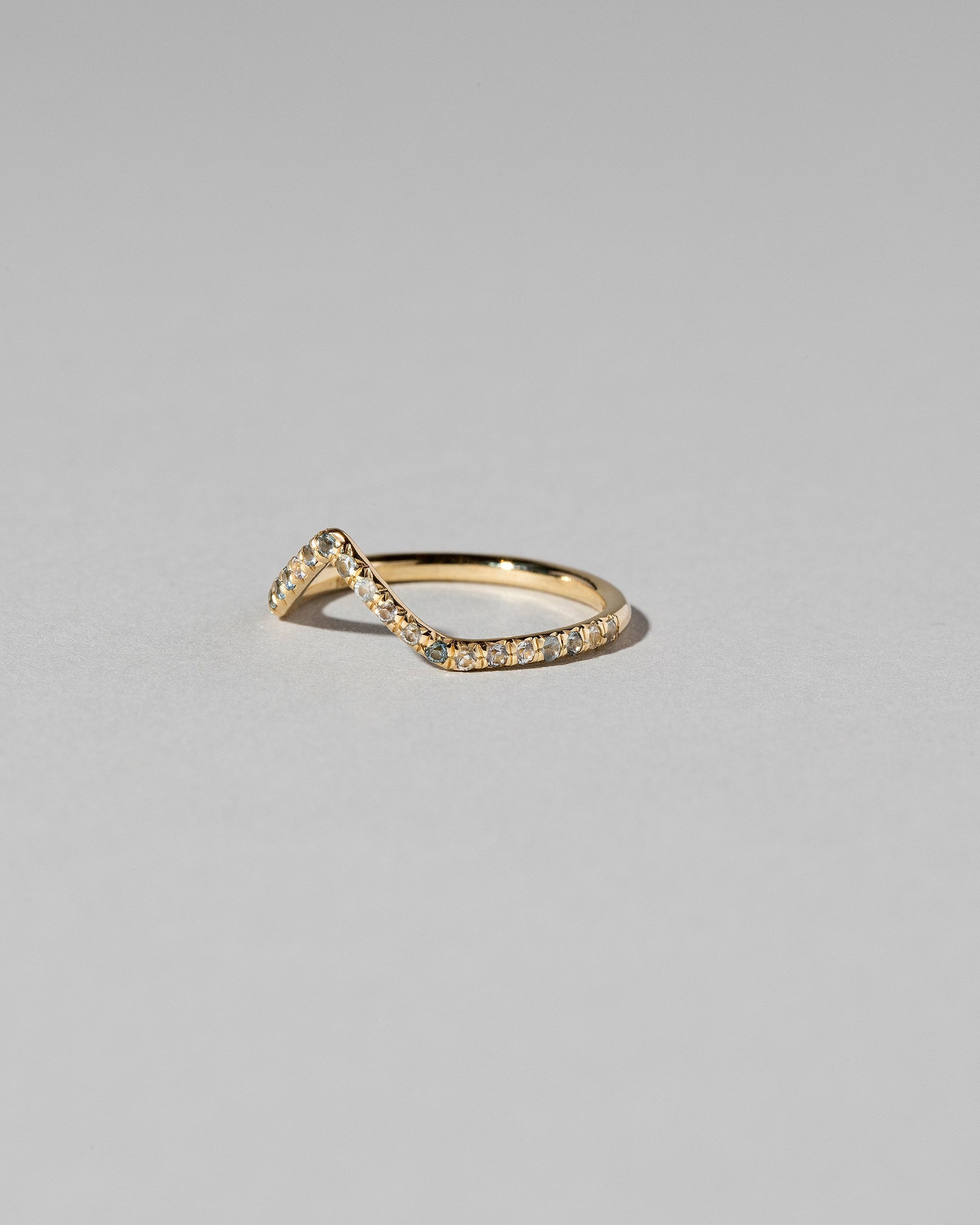 View from the side of the Gold Blue Sapphire Pavé High Peak Band on light color background.