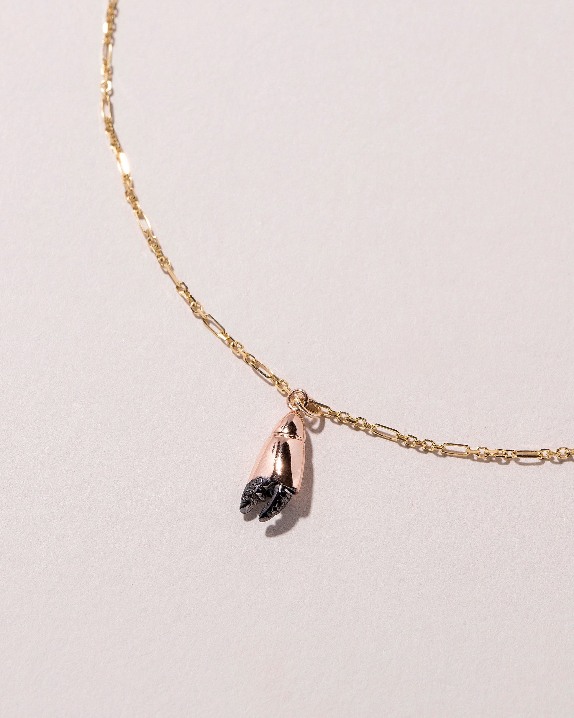 Closeup detail of the Stone Crab Claw Charm styled with the Abacus Chain Necklace on light color background.