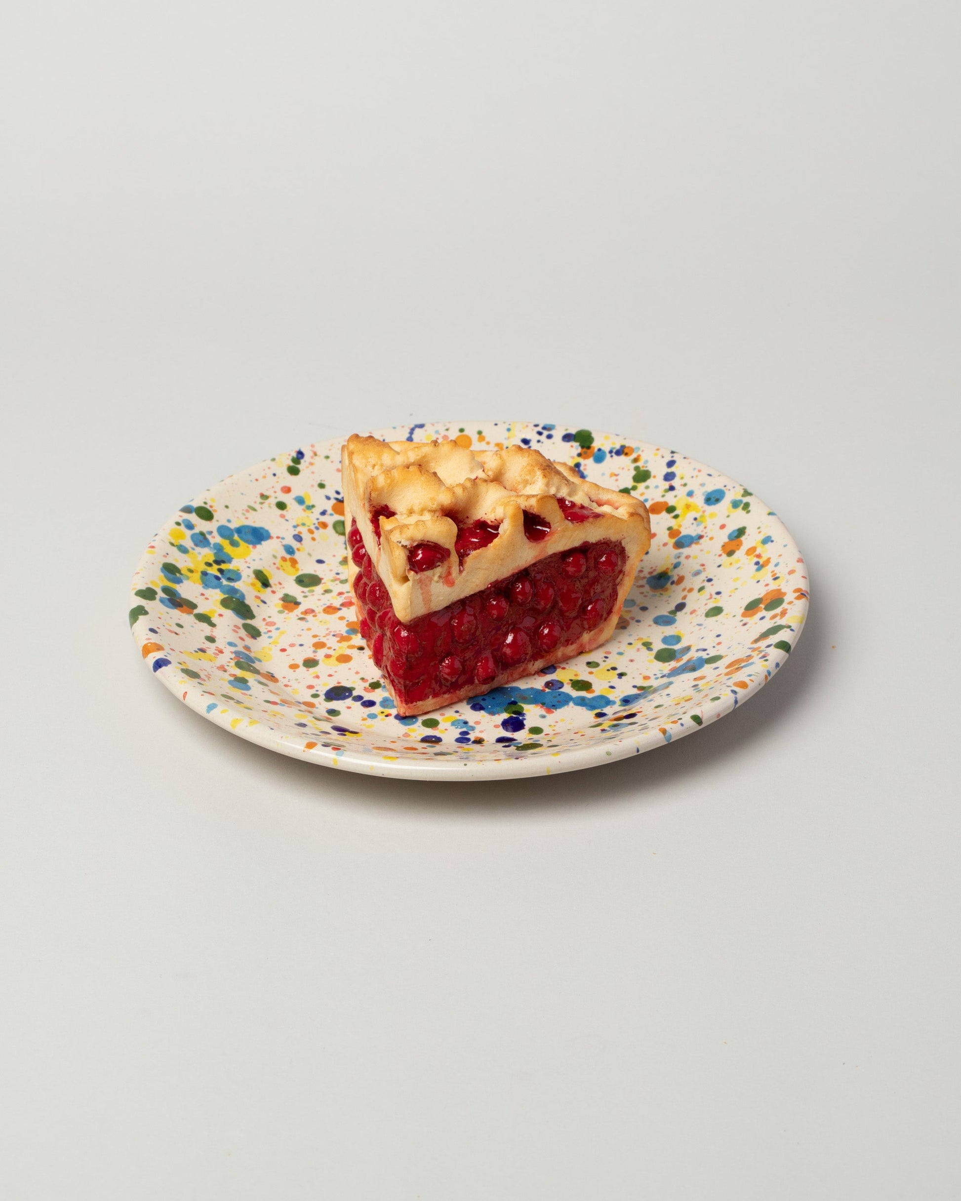 Detail view of the La Ceramica Vincenzo Del Monaco Colored Drops Medium Dish with a slice of cherry pie on light color background.