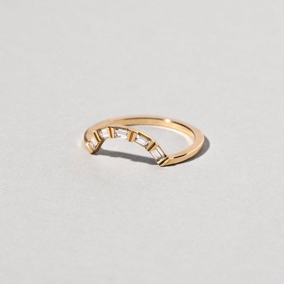 product_details::Closeup details of the Gold Baguette Curve Band on light color background.