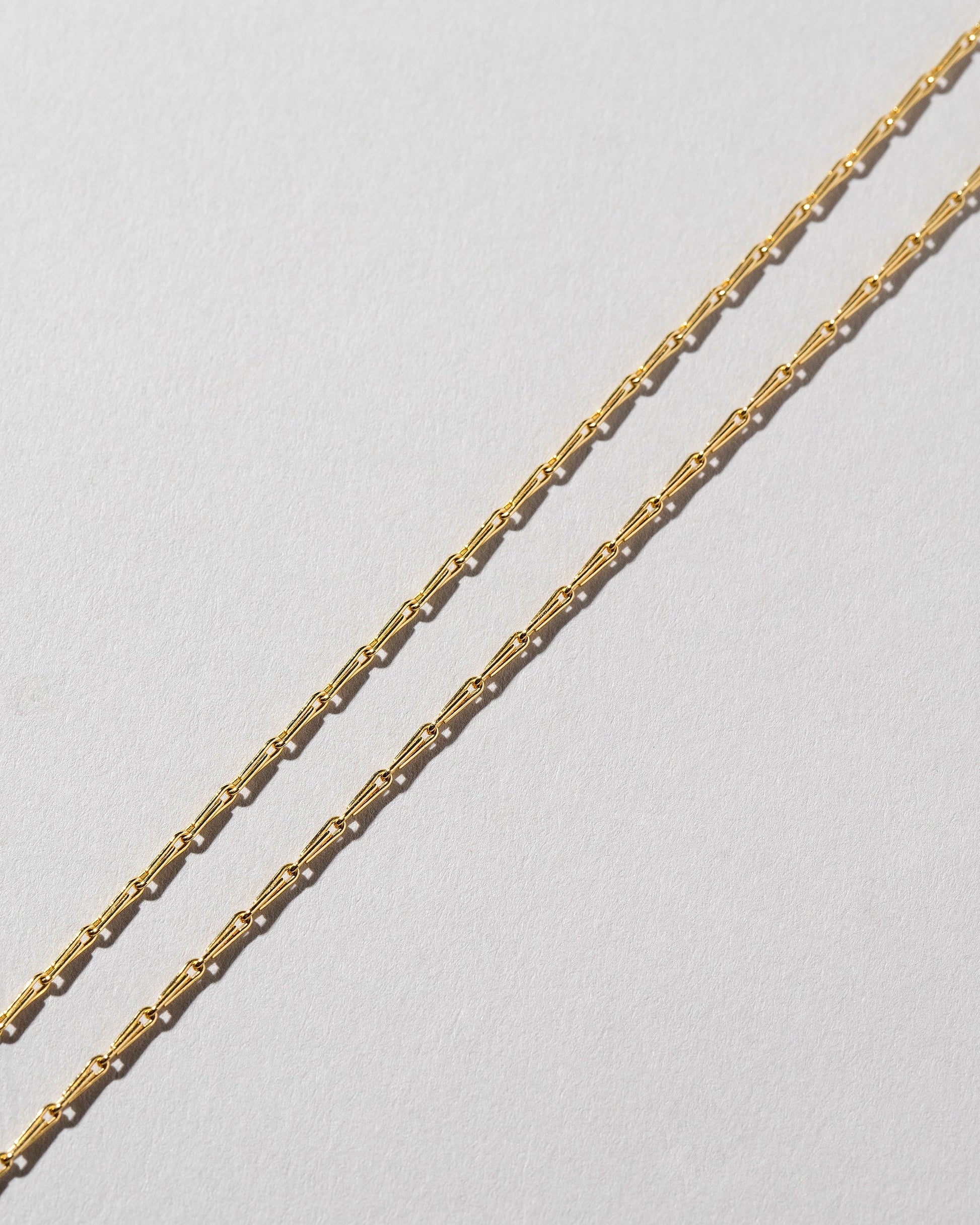 Closeup details of the Petite Pinched Loop Chain Necklace on light color background.