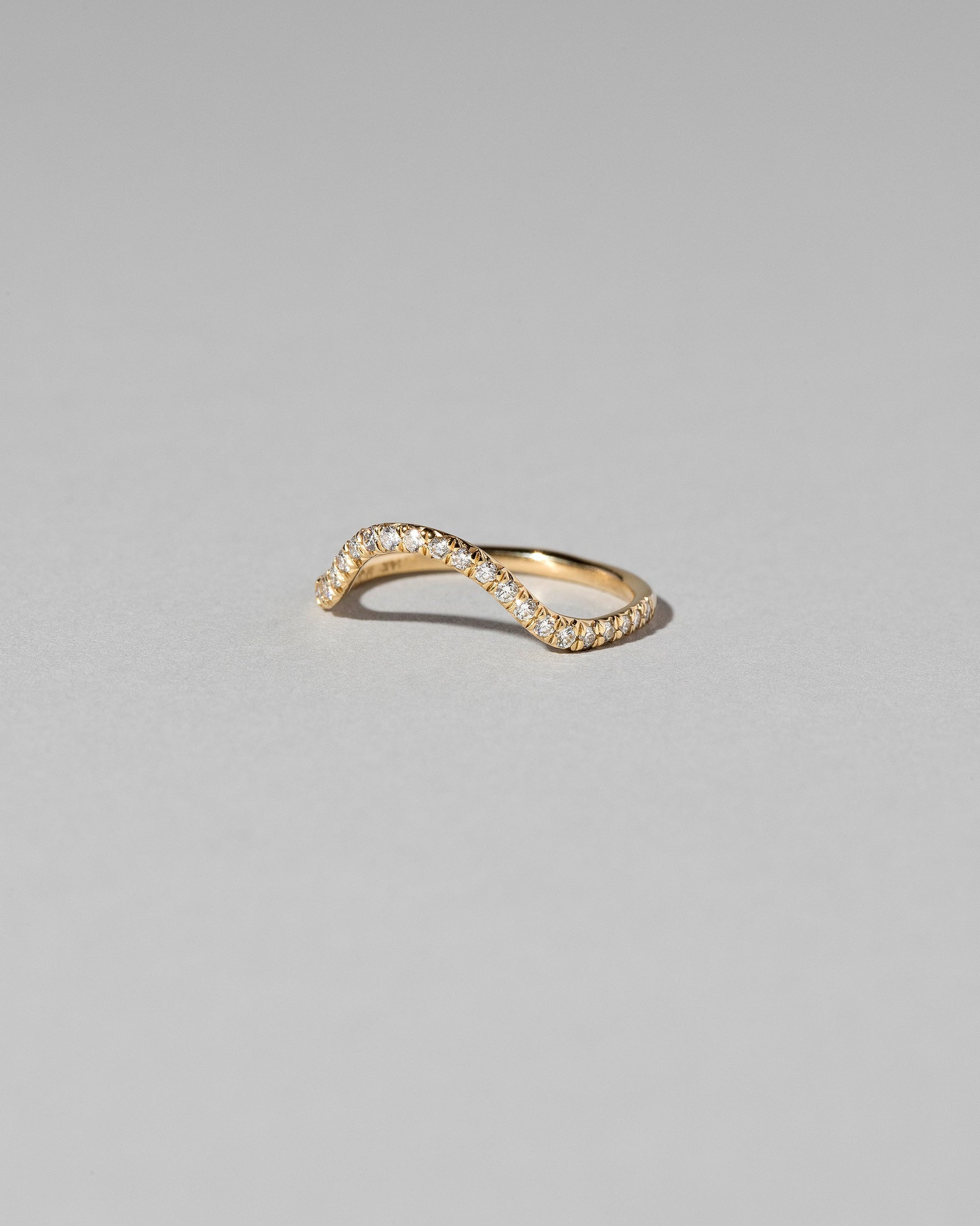 View from the side of the Gold White Diamond Sapphire Curve Band on light color background.