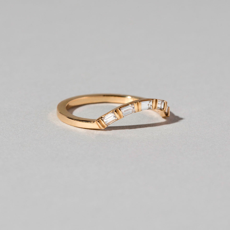 product_details:: Closeup details of the Gold Baguette Mini Curve Band on light color background.
