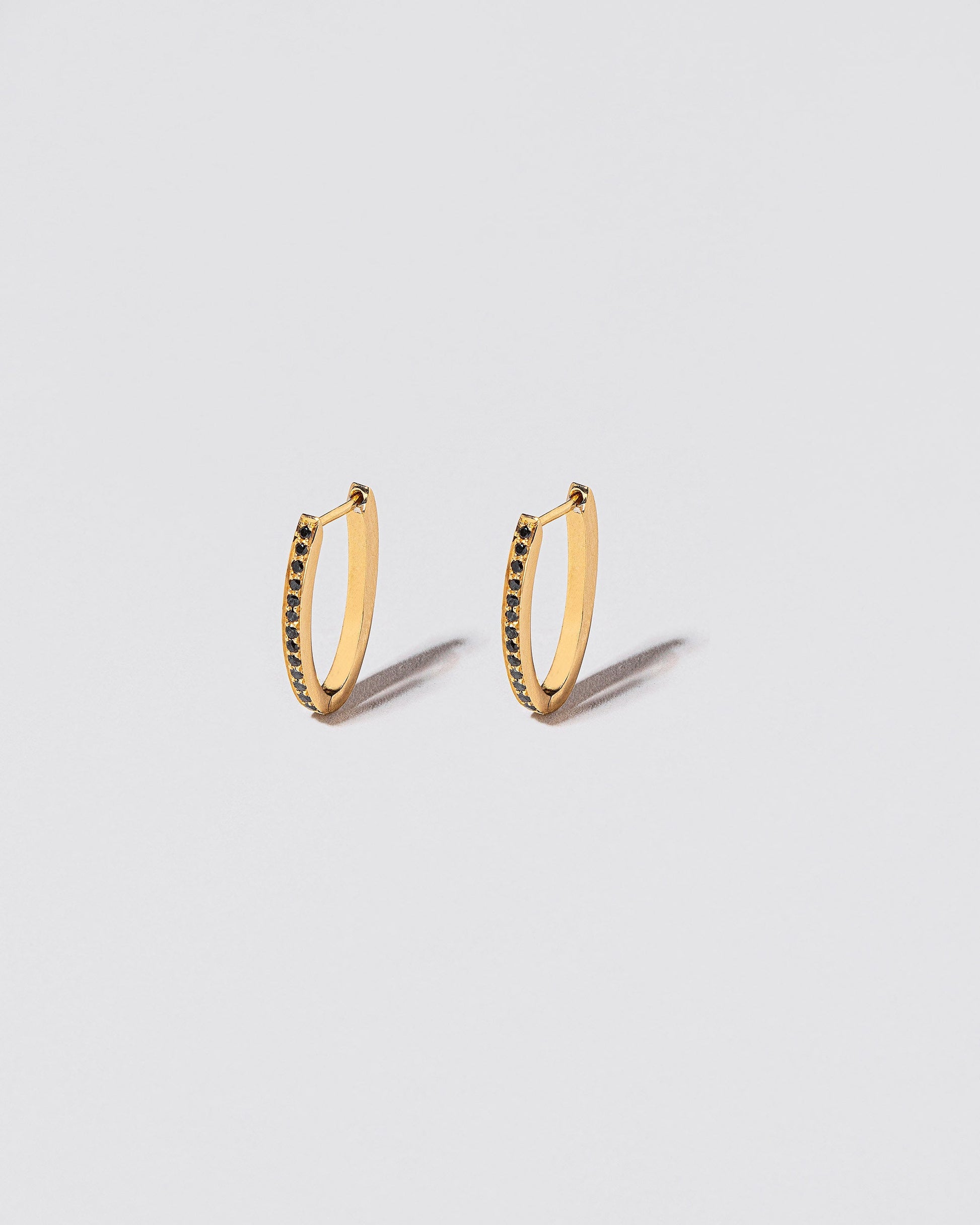 Gold Black Diamond Tiny Loop Hoop Earrings on light color background.